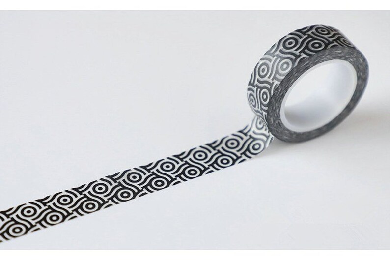 May include: A roll of decorative washi tape with a black and white geometric pattern. The tape is unrolled, revealing the repeating design of interlocking circles. The tape is on a white background.
