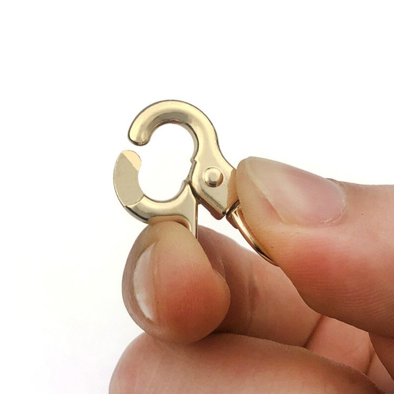 May include: Gold-toned metal swivel clasp with a spring-loaded gate. The clasp is designed for attaching to a bag, purse, or other accessories.