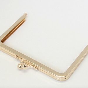 May include: Gold-toned metal purse frame with a rounded, double-clasp closure.
