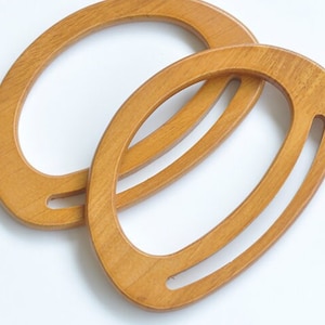 May include: Two wooden oval-shaped handbag handles. The handles are light brown and have a smooth finish.