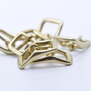 Pode incluir: Um close-up de um conjunto de quatro fivelas de metal dourado. As fivelas estão interligadas e têm um acabamento liso e polido.