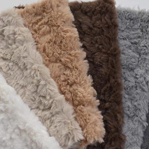 May include: A selection of faux fur fabric swatches in a range of neutral tones. The colours include white, cream, beige, brown, grey, and dark grey. The fabric has a soft, textured appearance.