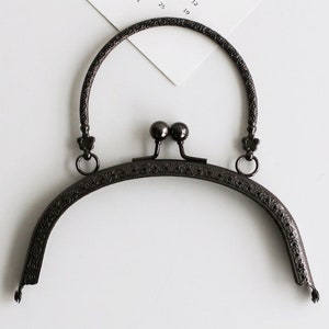 May include: Black metal purse frame with an ornate design and a rounded top handle.
