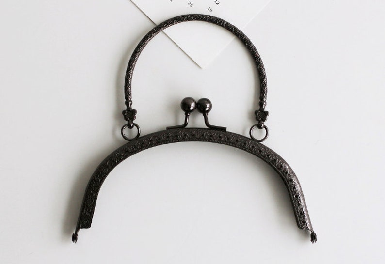 May include: Black metal purse frame with an ornate design and a rounded top handle.