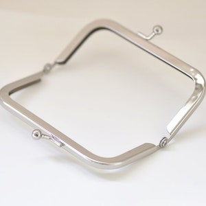 May include: Silver-toned metal purse frame with a square shape and two clasps.