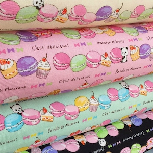 Op de afbeelding: Een stapel van vier stoffen panelen met een herhalend patroon van macarons, cupcakes en panda's. De stof is roze, groen en zwart. De tekst op de stof luidt "Macaron et fruits", "Panda et Macarons" en "C'est délicieux!"