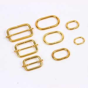 May include: A set of six gold-toned metal belt buckle slides in various sizes. The slides are oval and rectangular shaped.