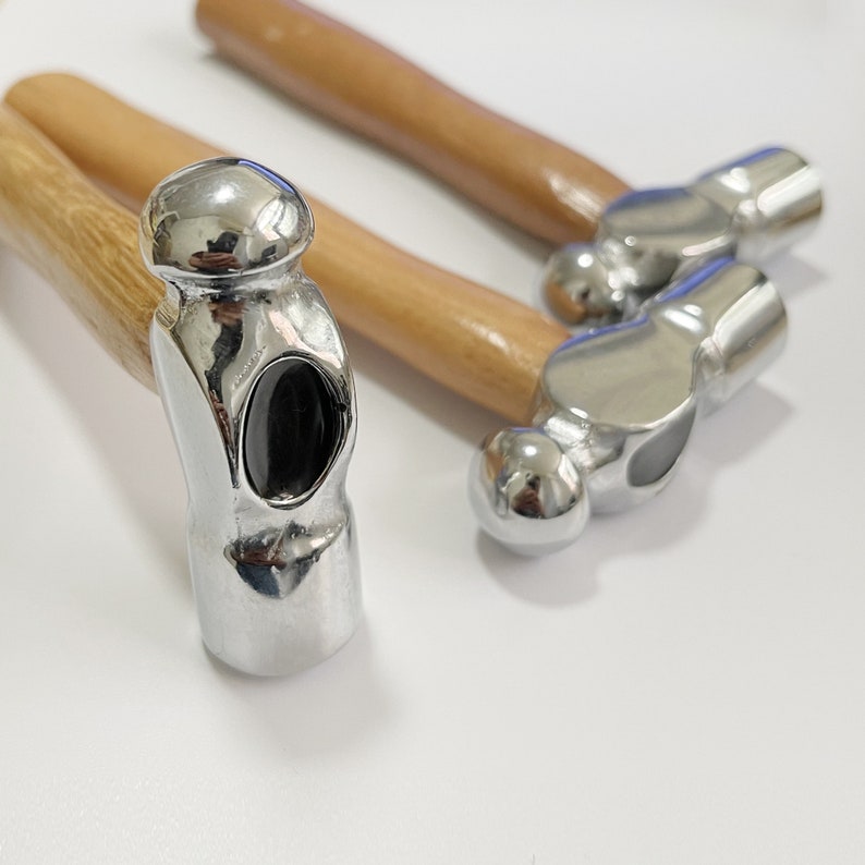 May include: Three silver-colored hammers with wooden handles. The hammers have round heads and are used for jewelry making.