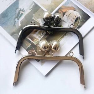 May include: Two purse frames, one gold and one black, with decorative ball clasps. The frames are made of metal and are designed to be used for handbags.