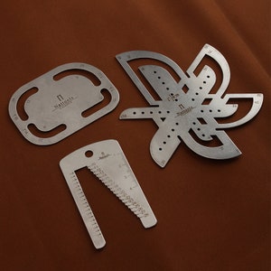 May include: Three metal tools for leather crafting. The tools are made by Nattools and include a ruler, a circle and a flower-shaped tool.