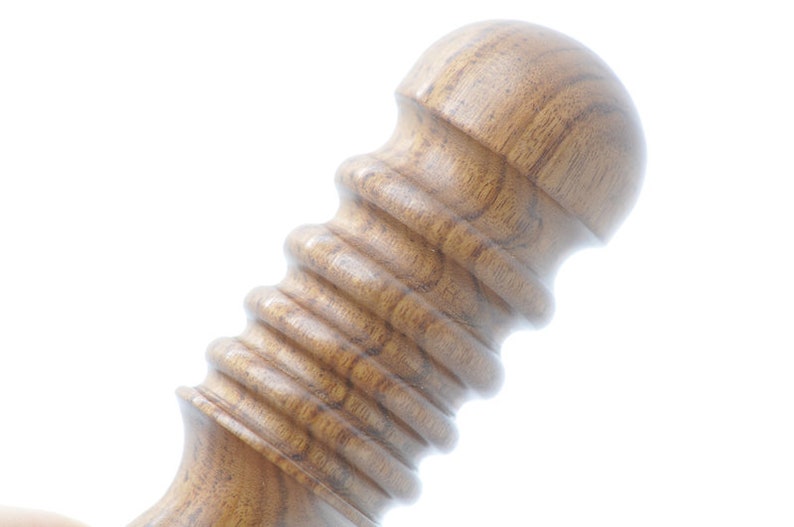 May include: Close-up of a wooden massage roller with a rounded top and a textured, ribbed surface.