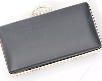 Può includere: Una pochette nera con cornice in metallo dorato e manico superiore in cristallo trasparente.