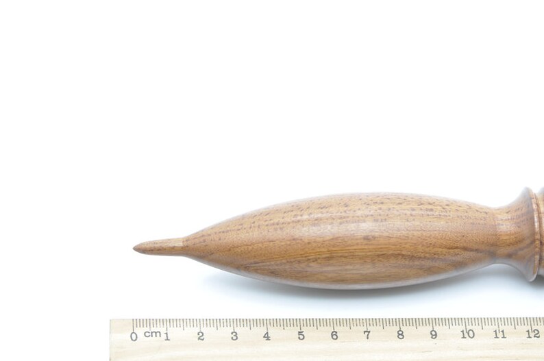 May include: A wooden spindle with a pointed tip and a rounded handle. The spindle is approximately 12 inches long and is made of a light brown wood.