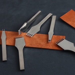 May include: Five different sized leather hole punches with multiple prongs on a brown leather strip. The punches are made of metal and have a silver finish.