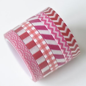 May include: A stack of six rolls of washi tape with different pink and white patterns. The patterns include stripes, zigzags, and a geometric design.