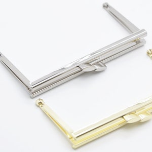 Puede incluir: Dos marcos de bolso de metal, uno plateado y otro dorado. Ambos marcos están cerrados y tienen forma rectangular.