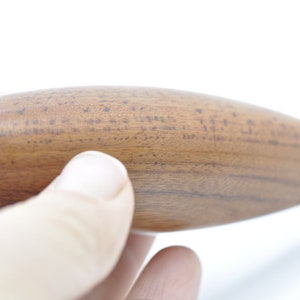 May include: Close-up of a wooden rolling pin with a smooth, brown surface. The rolling pin is held in a hand.
