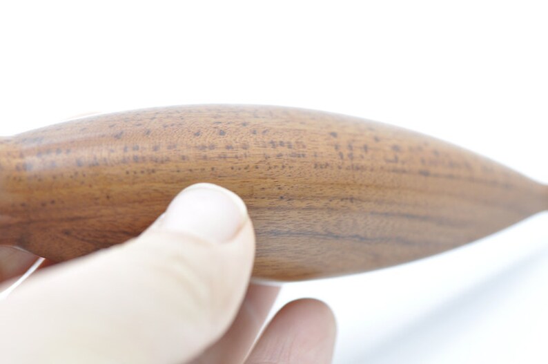 May include: Close-up of a wooden rolling pin with a smooth, brown surface. The rolling pin is held in a hand.