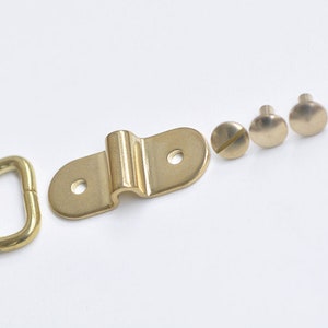 May include: A set of brass hardware for hanging items, including a D-ring, a hook, and four screws.