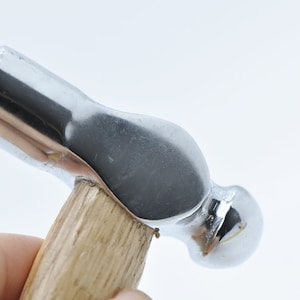 May include: A close-up of a silver ball-peen hammer with a wooden handle.