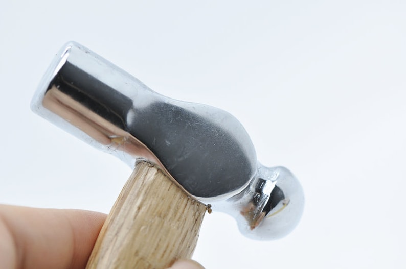 May include: A close-up of a silver ball-peen hammer with a wooden handle.