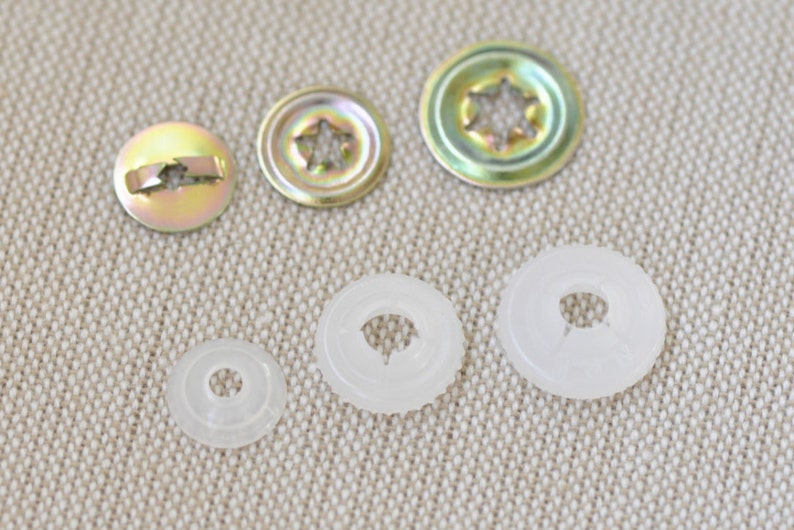May include: Assortment of metal and plastic snap fasteners in various sizes. The metal fasteners have a star-shaped opening and a gold finish. The plastic fasteners are white and have a round opening.