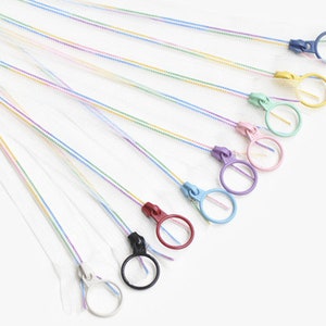 Könnte beinhalten: Eine Sammlung farbenfroher Reißverschlussanhänger mit passenden Ringgriffen. Die Reißverschlüsse haben einen Regenbogen-Schimmer, und die Anhänger sind in verschiedenen Farben erhältlich, darunter Blau, Gelb, Rosa und Lila. Die Anhänger sind an einer transparenten, dünnen Schnur befestigt.