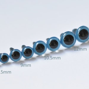 Op de afbeelding: Een set blauwe plastic veiligheidsogen met zwarte pupillen, variërend in grootte van 7,5 mm tot 12 mm. De ogen zijn in een lijn gerangschikt van de kleinste tot de grootste.