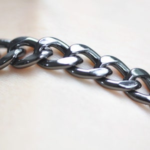Puede incluir: Un brazalete de cadena negro con eslabones grandes y planos.