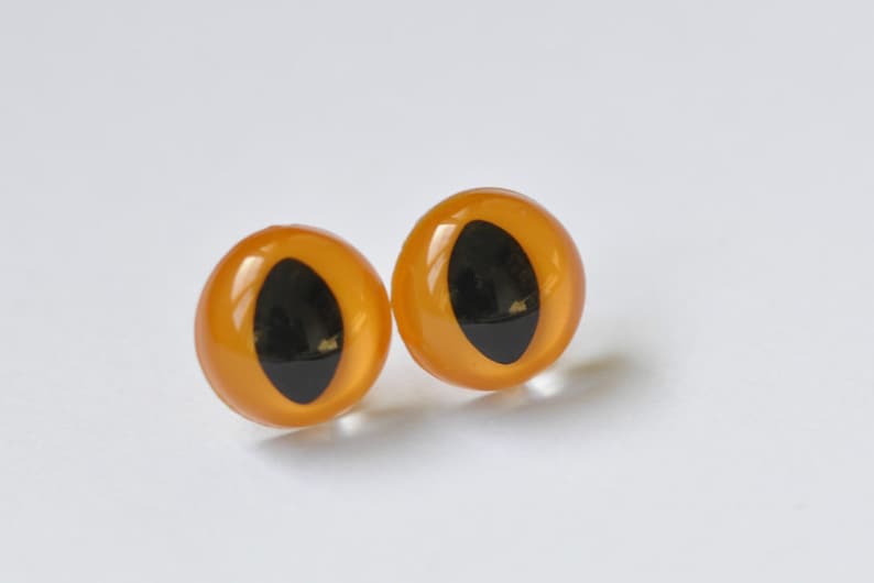 May include: Two orange plastic safety eyes with black pupils. The eyes are round and have a glossy finish.
