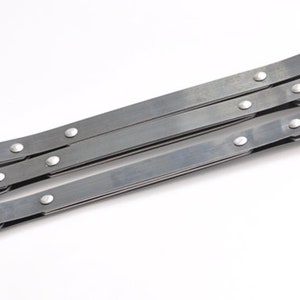 May include: A silver-toned, accordion-style metal object with multiple articulated sections. Each section is connected by rivets. The object is designed to expand and contract, and is set against a white background.