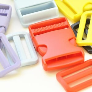 Puede incluir: Una colección de hebillas y deslizadores de plástico de colores en varios tonos, incluyendo rojo, amarillo, negro, morado y azul claro. Las hebillas tienen un diseño de cierre a presión, y los deslizadores tienen forma rectangular con tres ranuras. Probablemente se utilizan para correas o cinturones.