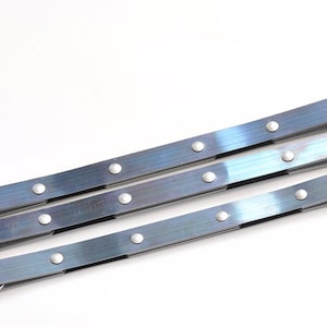 May include: Three silver metal straps with blue accents and silver rivets. The straps are arranged in a stack, with the top strap being the longest and the bottom strap being the shortest.