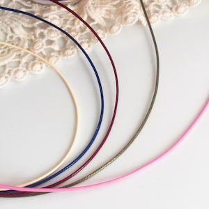 May include: Five spools of cord in different colors: pink, olive green, burgundy, navy blue, and cream.