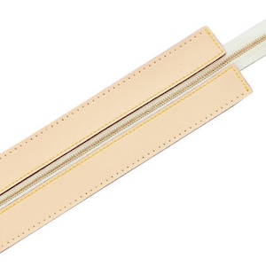May include: A beige leather zipper with a gold zipper pull. The zipper is sewn with yellow thread and has a dotted pattern.