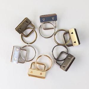 May include: Six silver, gold, and bronze key rings with a small rectangular loop on each. The loops have two small triangular cutouts.
