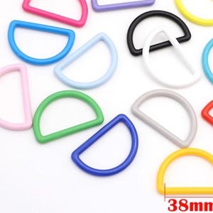 May include: A collection of colorful D-rings in various shades, including pink, blue, green, and yellow. The yellow D-ring measures 38mm across. These half-circle rings are made of a smooth, solid material.