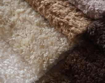 May include: Close-up of four different colors of fluffy faux fur fabric. The colors are white, light brown, brown, and pink.