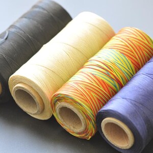 May include: Four spools of thread in different colors: black, beige, multi-colored, and purple. The spools are made of cardboard and have a wooden center.