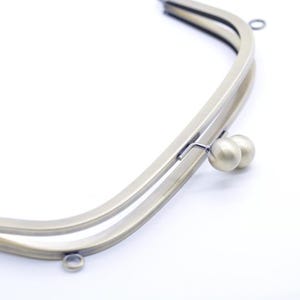 Puede incluir: Un marco de bolso curvo de latón antiguo con cierre de beso. El marco tiene un diseño de doble capa y pequeños bucles para sujetar a una bolsa. El cierre presenta dos pequeñas esferas redondas de color latón.