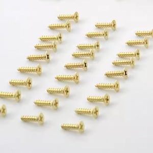 Puede incluir: Una colección de tornillos para madera de color dorado dispuestos en diagonal sobre un fondo blanco. Cada tornillo tiene una cabeza ranurada y un cuerpo roscado. Los tornillos están espaciados uniformemente, creando un patrón. La imagen está bien iluminada, resaltando el brillo metálico de los tornillos.