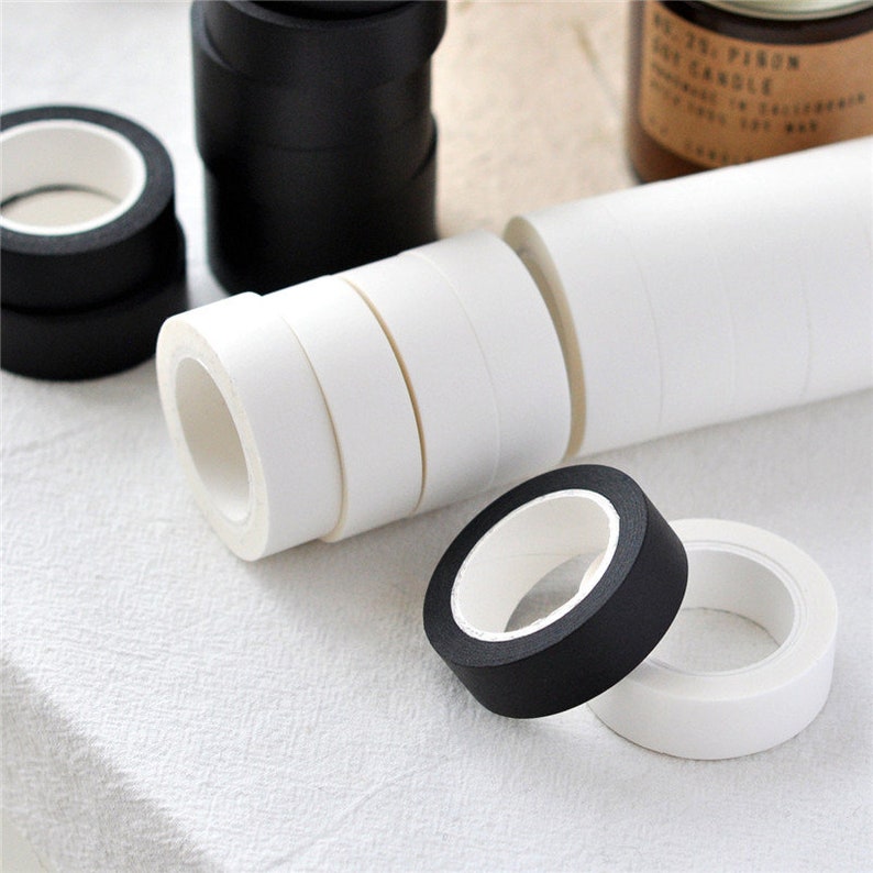 Puede incluir: Primer plano de rollos de cinta washi negra y blanca. Los rollos est&aacute;n apilados uno encima del otro. La cinta es un material de artesan&iacute;a popular que se utiliza para decorar, llevar un diario y hacer scrapbooking.