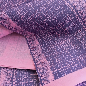 May include: Close-up of a pink and purple fabric with a textured pattern. The fabric is folded over itself, showing the different colors and patterns.
