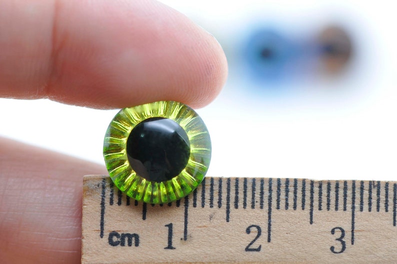 May include: A close-up of a green and black plastic safety eye, measuring 1 cm in diameter, for use in crafts and doll making.