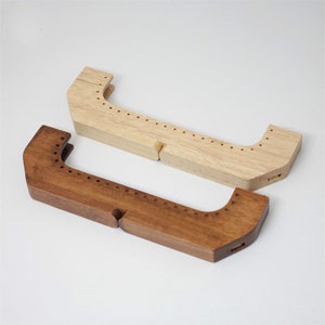 Könnte beinhalten: Zwei Holzhändel für Handtaschen, eines hellbraun und eines dunkelbraun. Beide Griffe haben eine Reihe von Löchern entlang der Oberseite und eine gebogene Form.