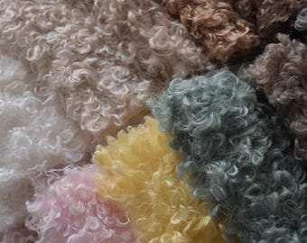 May include: Close-up of various curly textured fabrics in shades of white, pink, yellow, and blue-green. The fabrics have a soft, fluffy appearance, with tightly curled fibers. The arrangement of colors creates a visually appealing display of textures.