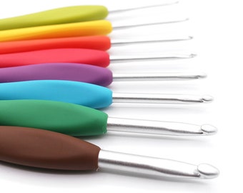 Puede incluir: Un juego de siete agujas de crochet de colores con puntas de metal plateado. Las agujas están dispuestas en orden de arcoíris, comenzando por el verde y terminando por el marrón.