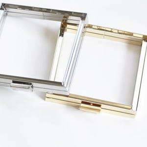 May include: Two rectangular metal purse frames, one in a polished silver tone and one in a gold tone. Each frame features a hinged construction with a central rectangular clasp mechanism for opening and closing the frame securely.