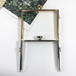 May include: Two metal purse frames, one gold and one silver, with a square shape and a clasp closure. The frames are open and ready to be used for a DIY purse project.