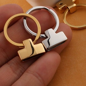 May include: Two keychains with a gold and silver finish. The keychains have a round ring and a T-shaped metal piece.